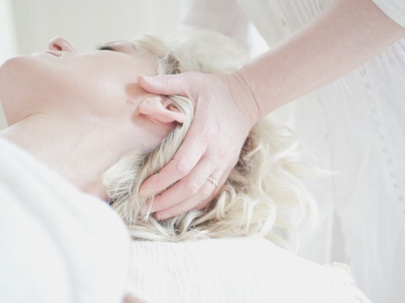 Into Balance Therapies offers CranioSacral Therapy - Image of blonde lady lying on her back with hands on her skull
